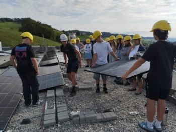 Jugendliche helfen mit, eine Solaranlage auf dem Schulhausdach zu installieren