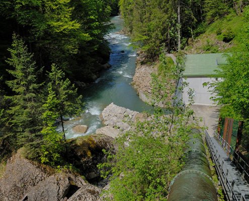 Druckleitung von Wasserkraftwerk neben Fluss im Wald